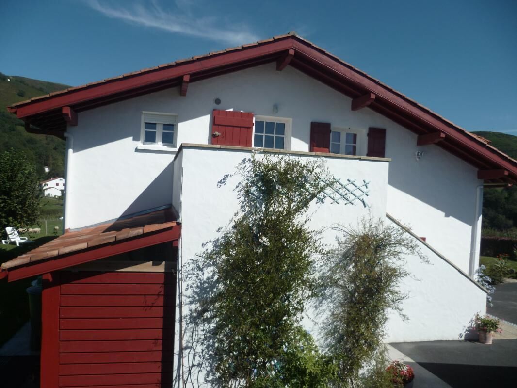 Un bâtiment blanc avec un toit rouge et deux fenêtres dotées de volets rouges.