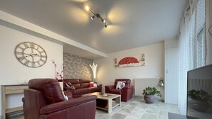 A modern living room with a leather sofa, a coffee table, and a TV stand. There is a brick wall and a decorative clock on the wall. - Uharte Beherea - Souraide (SOURAIDE)