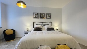 A neatly arranged bedroom with a large bed, bedside lamps, a black chair, and a hanging light fixture. - Uharte Beherea - Souraide (SOURAIDE)