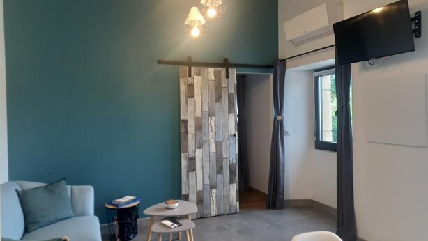 Una habitación moderna con una pared verde azulado, un sofá gris, una mesita redonda pequeña, un televisor montado en la pared y un separador de madera.
