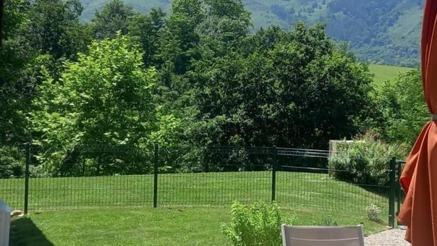 Un patio con tavolo e sedie, vista su un paesaggio verde con alberi e una montagna sullo sfondo.