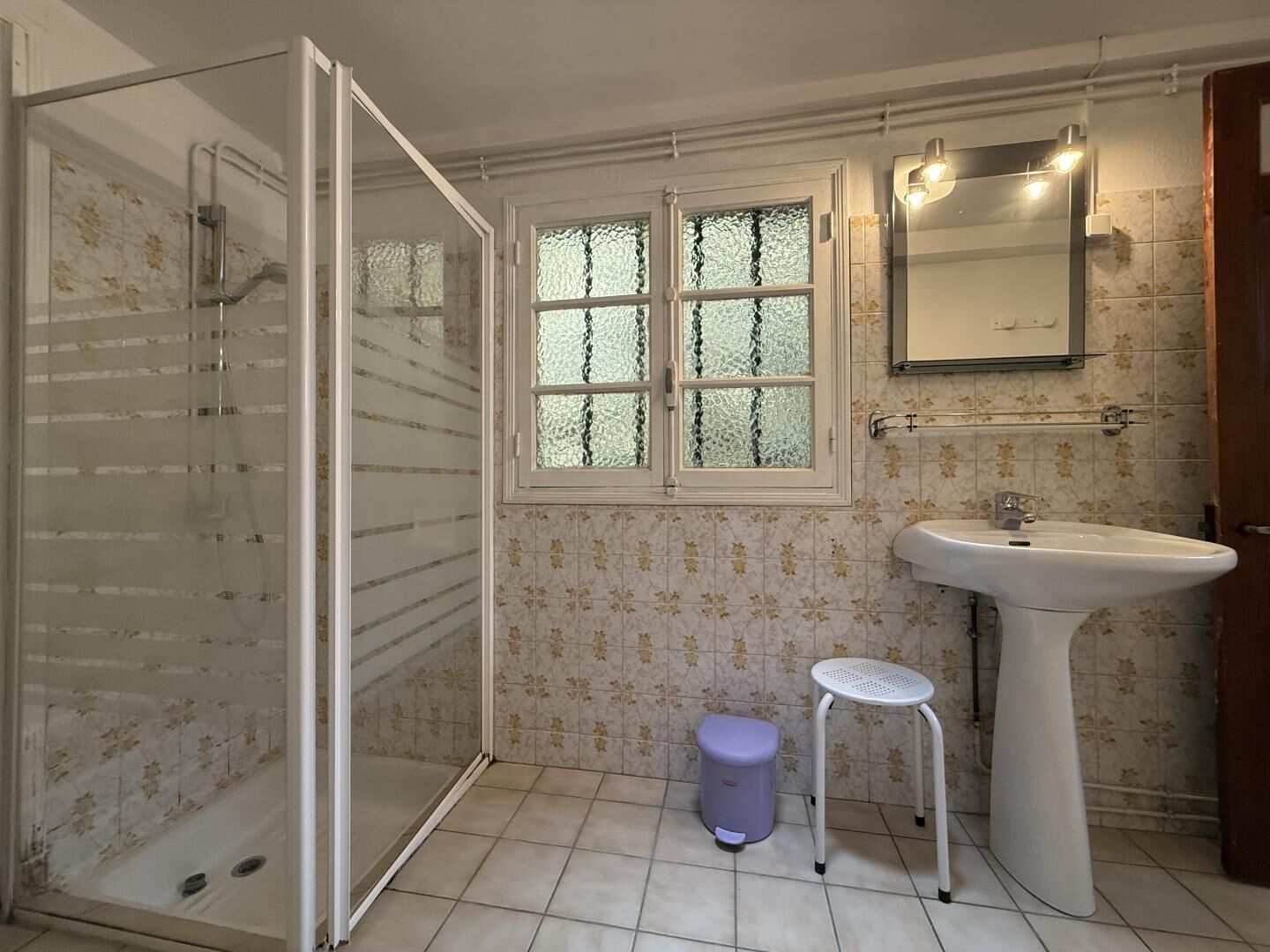 Uma casa de banho com chuveiro, pia, sanita e janela com vidro jateado.