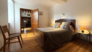 Een slaapkamer met een houten bed, een stoel, een nachtkastje met een lamp en een open haard op de achtergrond.