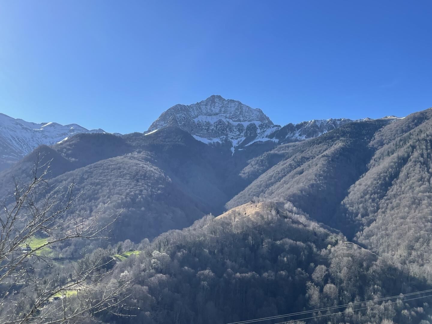 A mountainous landscape with a prominent peak, forested valleys, and a clear sky.