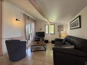 A living room with a sofa, armchair, TV, and a window with curtains.