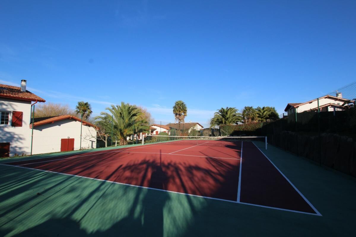 An outdoor tennis court surrounded by houses and palm trees.