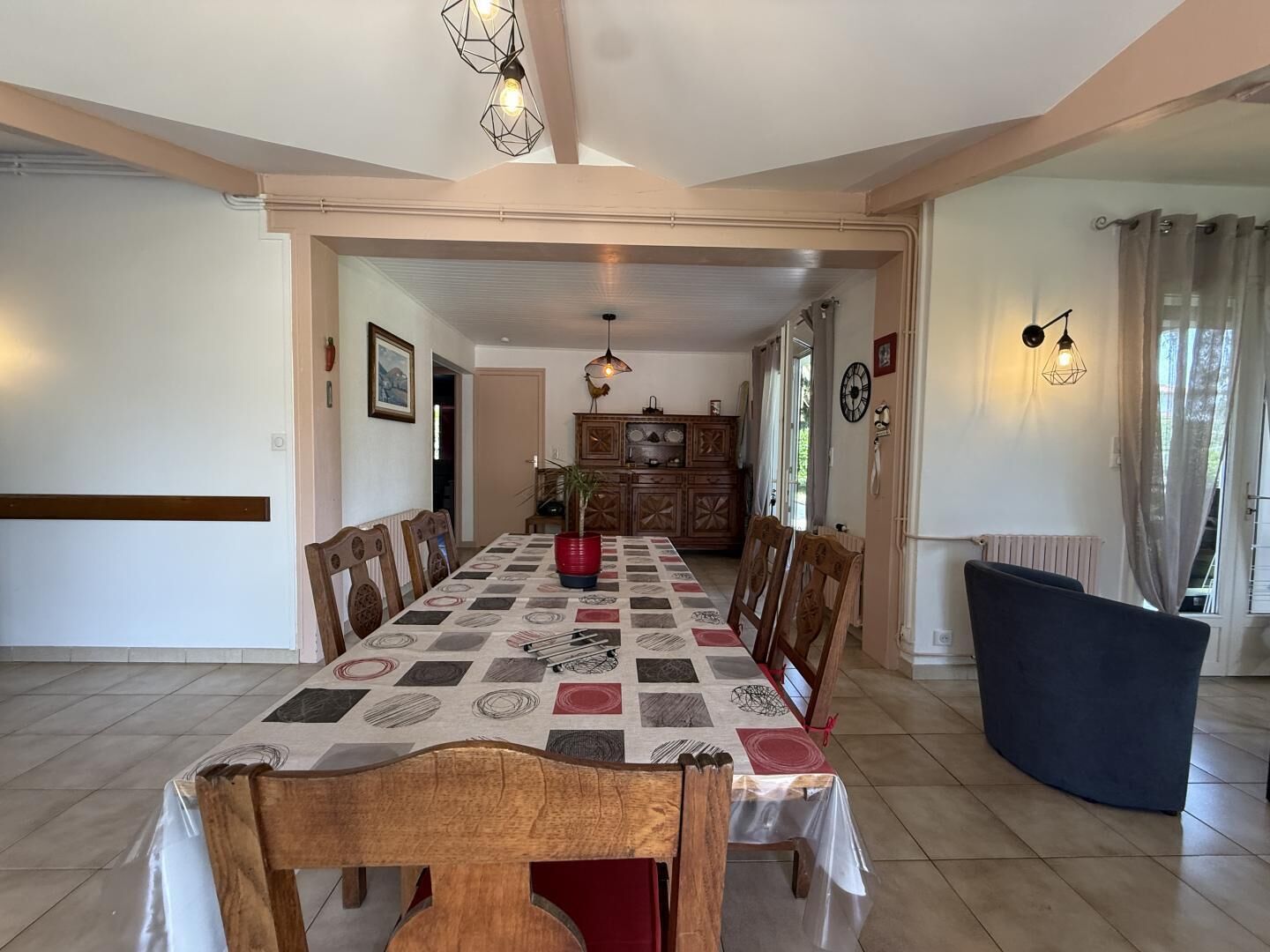 A dining area with a long table, chairs, a cabinet, and a blue sofa.