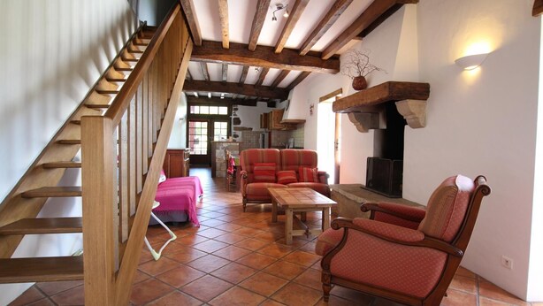 A spacious living area with a wooden staircase, red upholstered chairs, a wooden table, and a fireplace. - Zamatelua 2 - Sare - Gîte (SARE)