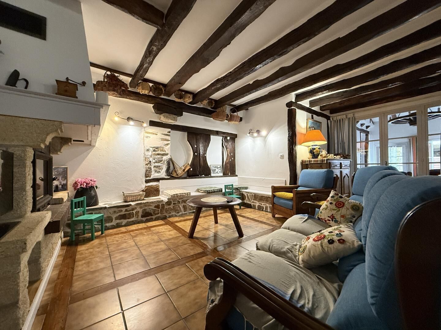 Een gezellige woonkamer met zichtbare houten balken, een stenen open haard en een blauwe bank.