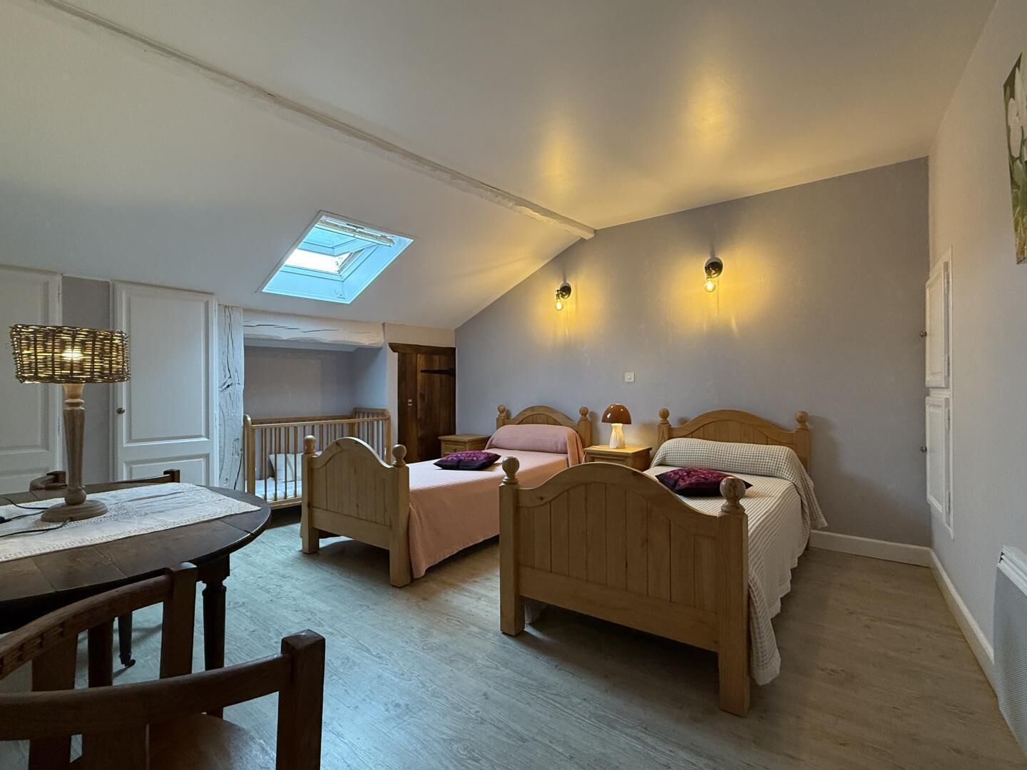 Une chambre avec deux lits en bois, une lucarne et un coin repas comprenant une table et des chaises.