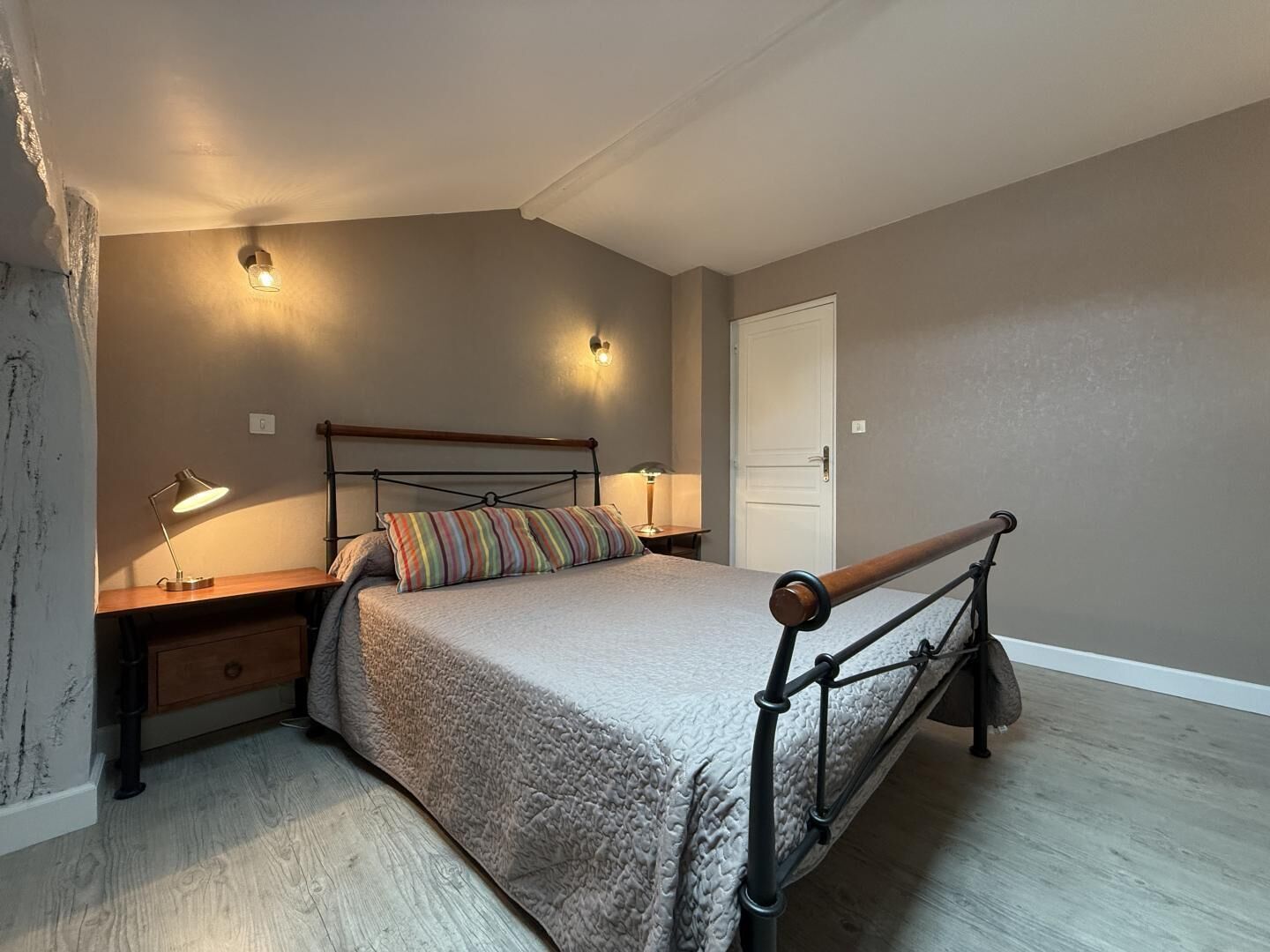 A bedroom with a bed, bedside lamps, a nightstand, and a door.