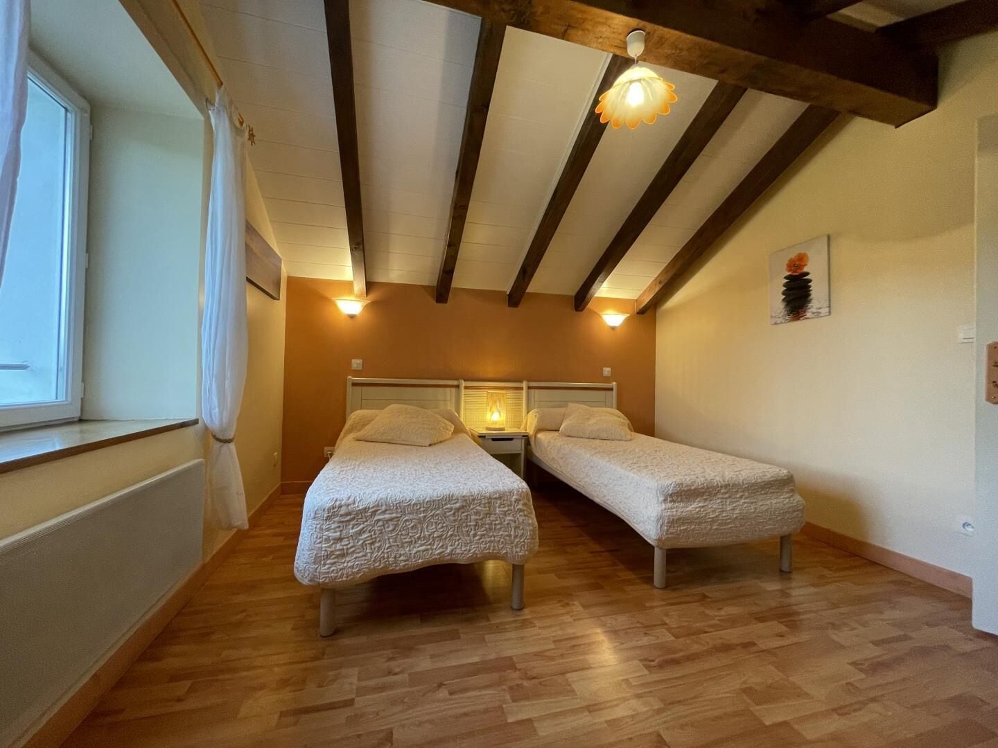 A room with two single beds, wooden flooring, exposed beams, and a window with curtains.