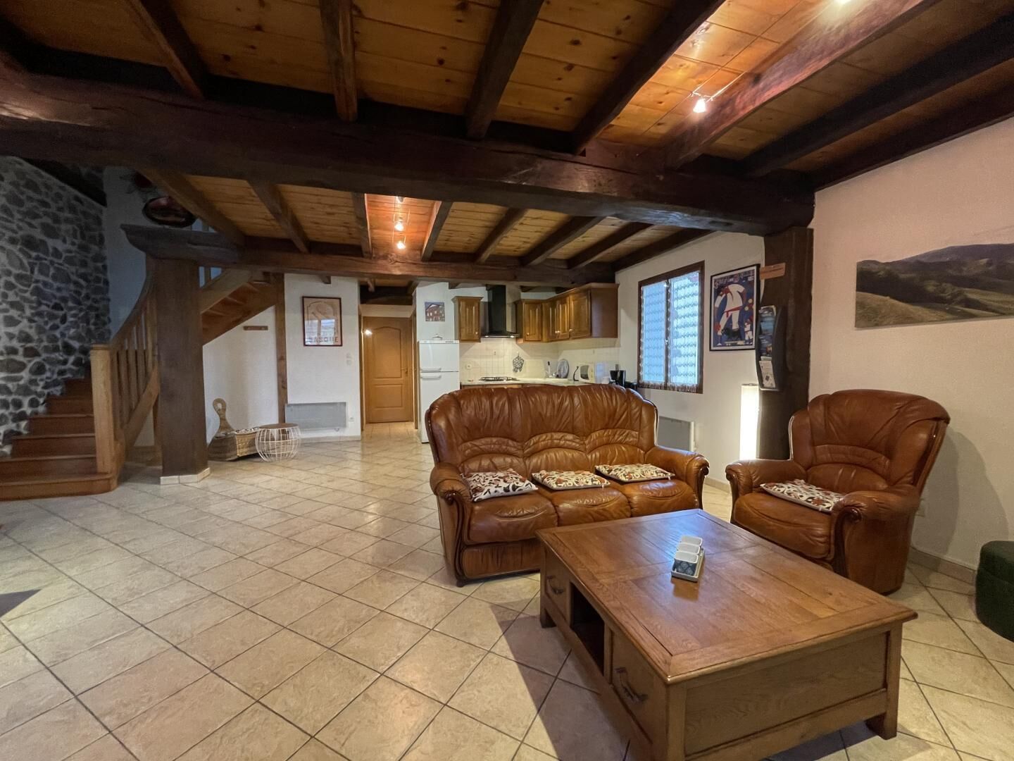 Een ruime woonkamer met een houten plafond, een stenen muur, een bank, een fauteuil en een salontafel.