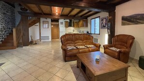A spacious living area with a wooden ceiling, a stone wall, a sofa, a chair, and a coffee table. - Haizalde - Saint-jean-le-vieux (SAINT-JEAN-LE-VIEUX)