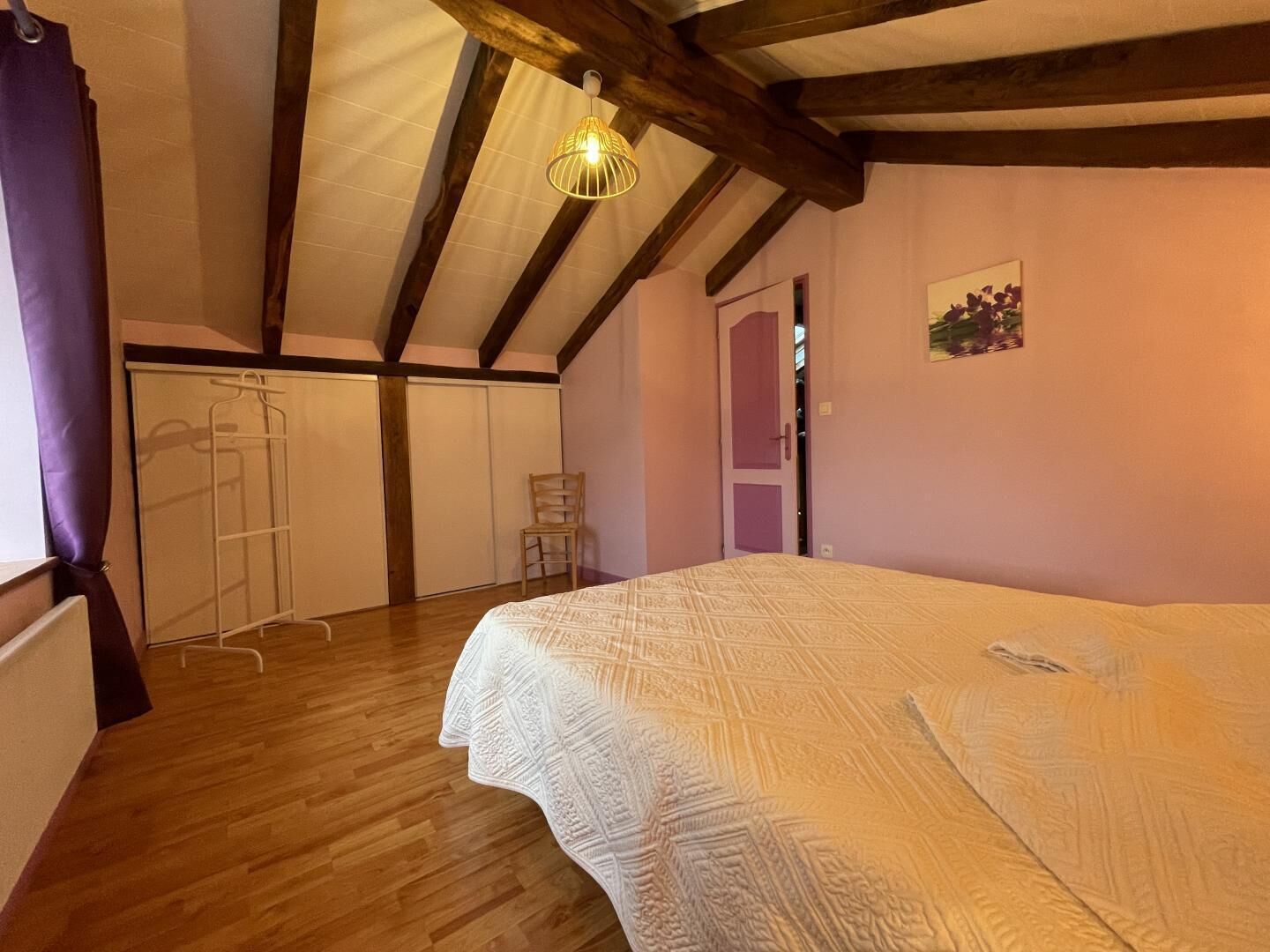 Un dormitorio con techo de madera, una cama con colcha estampada, una silla, un armario y una lámpara colgante.