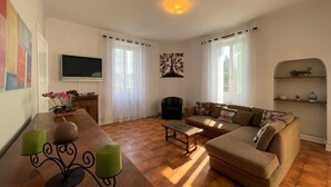 A living room with a sofa, a coffee table, a TV, and a dining table with candles. - LACAZE-BUSQUET - GELOS (GELOS)