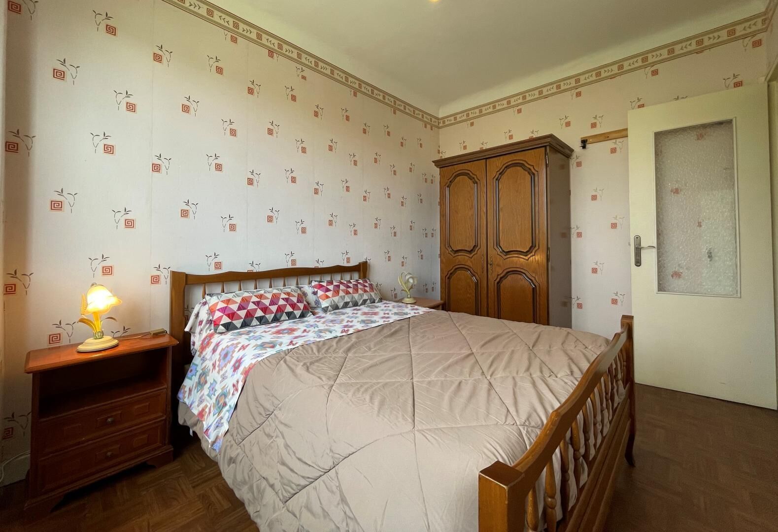 Une chambre à coucher avec un lit, une armoire en bois, une table de chevet et une lampe.