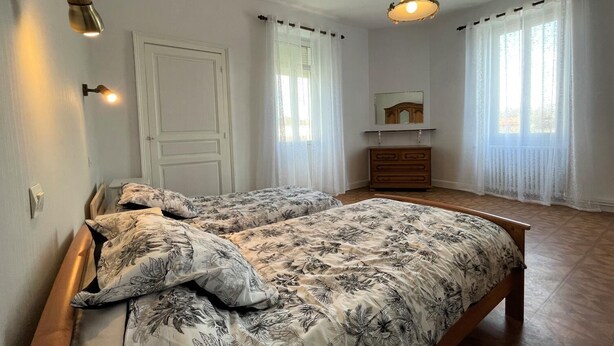 A bedroom with two beds, a wooden dresser, a mirror, and a hanging light fixture. - LACAZE-BUSQUET - GELOS (GELOS)