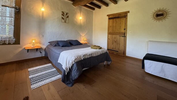 Un dormitorio con cama, lámparas de noche, un armario de madera, una ventana con cortinas de encaje y suelo de madera.