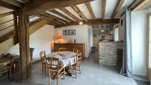 Una cocina rústica con vigas de madera a la vista, un revoque de piedra y una zona de comedor con una mesa redonda y sillas.