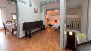 A spacious living area with a dark wooden bench, a dining table with chairs, and a white bed in the background. - Haizteia - Saint-pee-sur-nivelle (SAINT-PEE-SUR-NIVELLE)