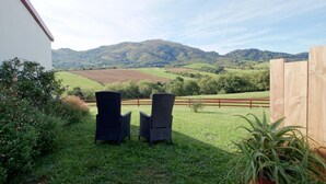 A patio with two chairs and a wooden fence, overlooking a green field and hills. - Xokoan - Sare - Gîte (SARE)