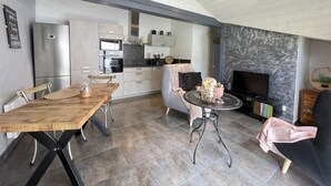 A modern kitchen with built-in appliances, a dining area with a wooden table and chairs, and a seating area with a sofa and a TV. - Xokoan - Sare - Gîte (SARE)