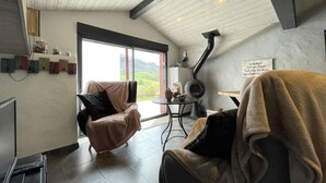 A cozy living room with a high ceiling, a fireplace, a comfortable chair, and a view of the outdoors. - Xokoan - Sare - Gîte (SARE)
