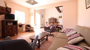 A living room with a sofa, armchairs, a coffee table, a TV on a wooden cabinet, and a dining area with chairs and a table. - Ur-ondoa - Larceveau (LARCEVEAU)
