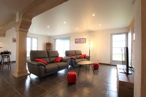 A spacious living room with two sofas, a coffee table, and a red ottoman. - Airosa - Sare - Gîte (SARE)