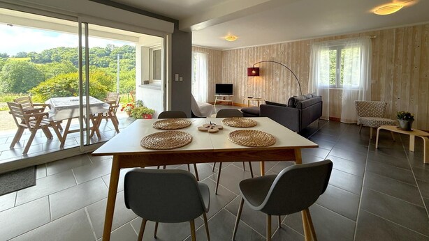 Un salon moderne avec un coin repas, de grandes fenêtres et une vue sur la verdure.