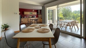 Un coin repas avec une table dressée pour six personnes, une cuisine en arrière-plan et une porte-fenêtre coulissante donnant sur une terrasse extérieure.