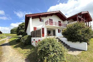 Una casa a due piani con un balcone, un portico coperto e un sentiero sterrato che conduce all'ingresso.