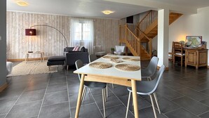 Un grand espace de vie comprenant une table à manger, des chaises, un canapé, un escalier et un petit coin bureau.