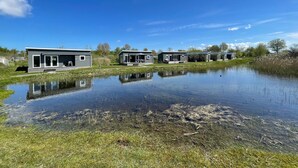 Filas de cabañas modernas de un solo piso con ventanas amplias, ubicadas junto a un estanque tranquilo con reflejos nítidos.
