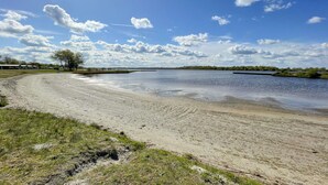 Una playa arenosa con un río tranquilo, árboles y un cielo despejado.