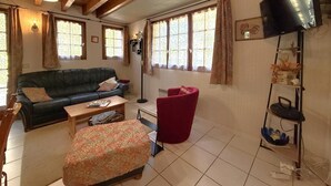 A living room with a sofa, armchair, ottoman, and a television mounted on the wall.