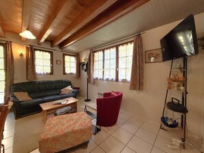 A living room with a sofa, armchair, ottoman, and a television mounted on the wall. - Cauhape - Auga - Gîte (AUGA)