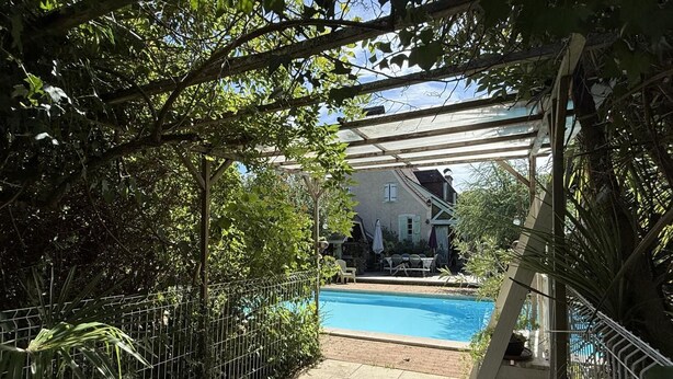 A pool area with a pergola, a fenced garden, and a house in the background.