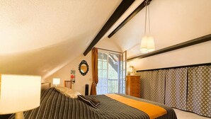 A bedroom with a bed, a bedside table with a lamp, a dresser, and a window with curtains.