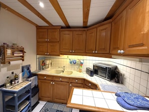 A kitchen with wooden cabinets, a sink, a coffee maker, a toaster, and a microwave. - Cauhape - Auga - Gîte (AUGA)