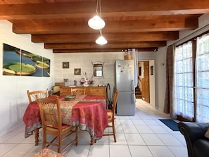 A dining area with a wooden table and chairs, a refrigerator, and a kitchen in the background. - Cauhape - Auga - Gîte (AUGA)