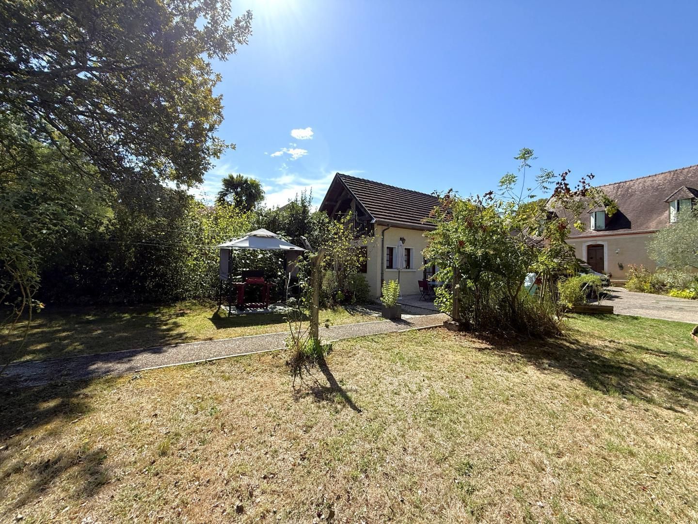 A residential property with a covered outdoor seating area, a pathway leading to the house, and a well-maintained lawn.