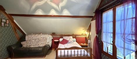 A bedroom with a wooden bed, a sofa, a nightstand, and a window with curtains.