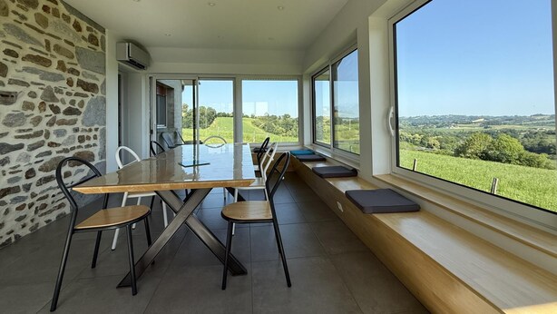Un comedor con una mesa larga, sillas y vistas a un paisaje verde a través de ventanas amplias.
