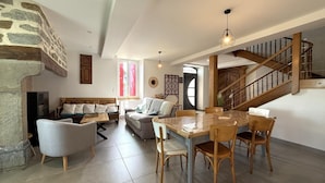 Amplia sala de estar con pared de piedra, una escalera de madera y una mesa de comedor con sillas.
