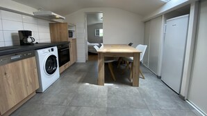 A compact kitchen with a washing machine, a coffee maker, and a dining area with a table and chairs. - Mendi Bichta - Halsou (HALSOU)