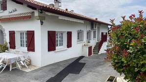 A white building with red shutters, a tiled roof, and a staircase leading to a second floor. - Mendi Bichta - Halsou (HALSOU)