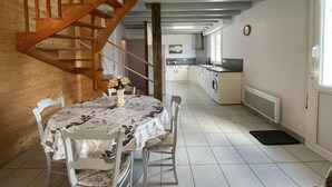 A dining area with a table and chairs, a wooden staircase, a kitchen with a washing machine, and a radiator.