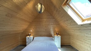 A bedroom with a sloped ceiling, wooden walls, a bed with a white bedspread, two bedside tables with lamps, and a skylight.